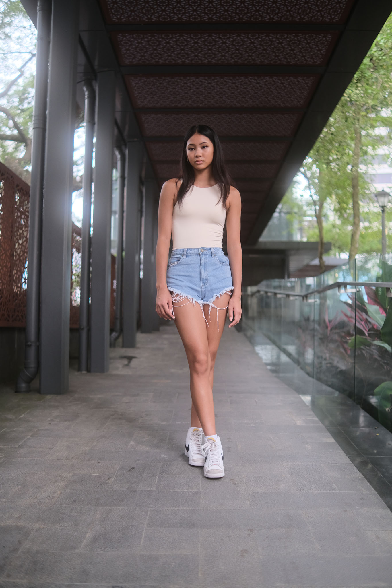 Full-body shot of a woman standing with one foot crossed in front of the other, hands in pockets—an easy, stylish pose for women’s street photography